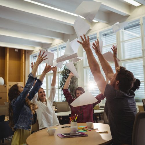 Group of excited business executives throwing paper and having fun in office